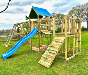 Grande aire de jeux en bois avec toboggan, mur d'escalade, pont de singe et balançoires sur une pelouse